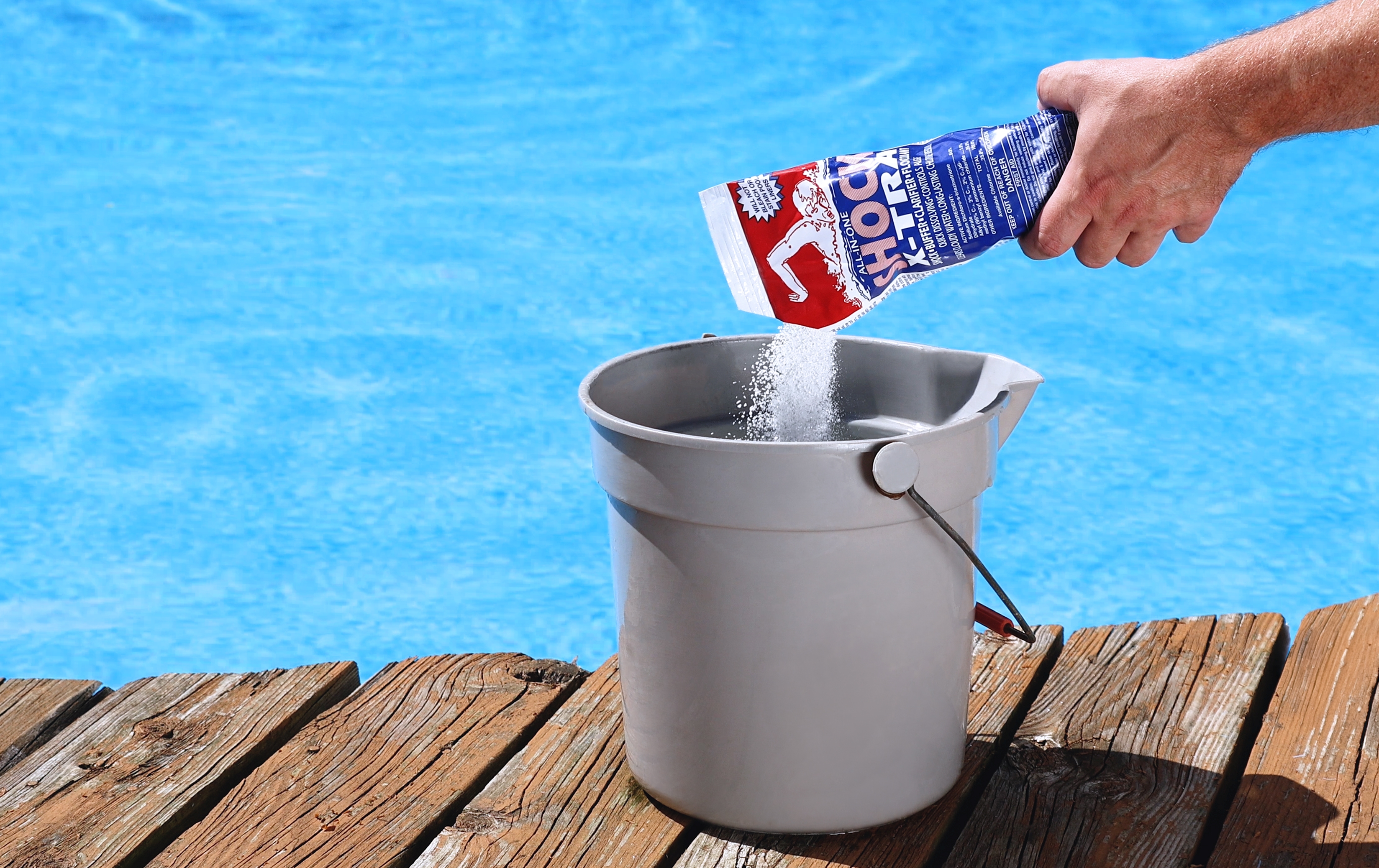 A person pouring shock into a bucket before putting it in their pool